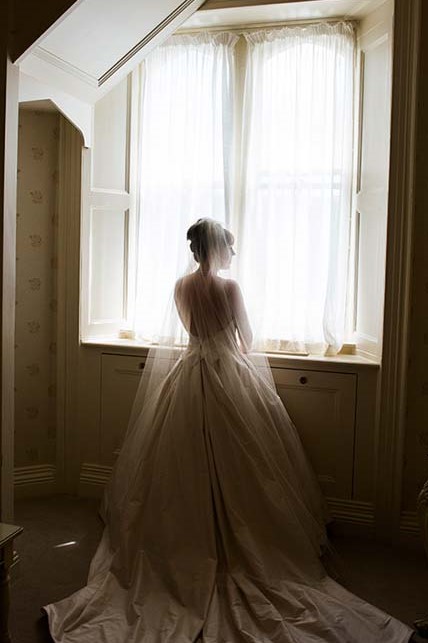 Bride staning in front of a window with a chapel veil