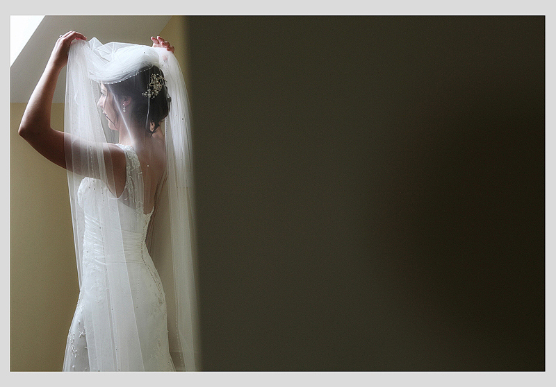 Bride pushing back her veil standing in front of a window